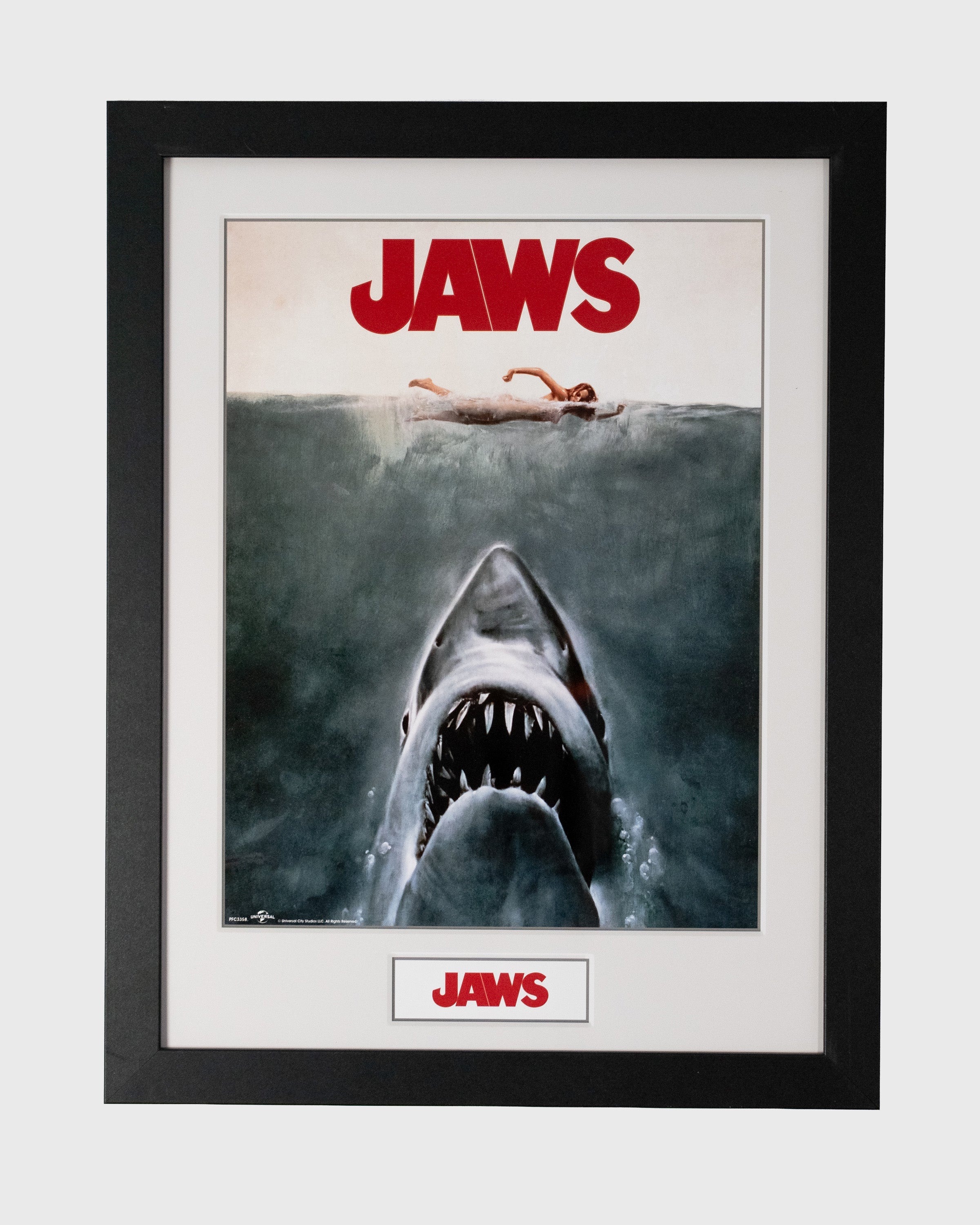 Plakat Jaws w czarnej ramie z rekinem wynurzającym się spod wody